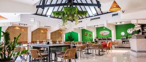 A spacious restaurant with high ceilings, hanging plants, and a variety of seating arrangements.