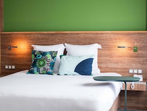A hotel room with a wooden headboard, a bed with white bedding, and two decorative pillows. - Ibis Styles Cayenne Centre Amazonia (Ouverture Juin 2024) (Cayenne)