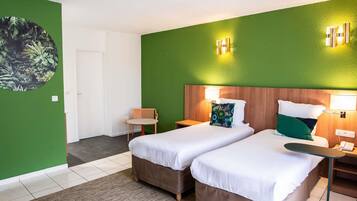 Une chambre d’hôtel avec deux lits, un mur d’accent vert, un miroir rond et une petite table.