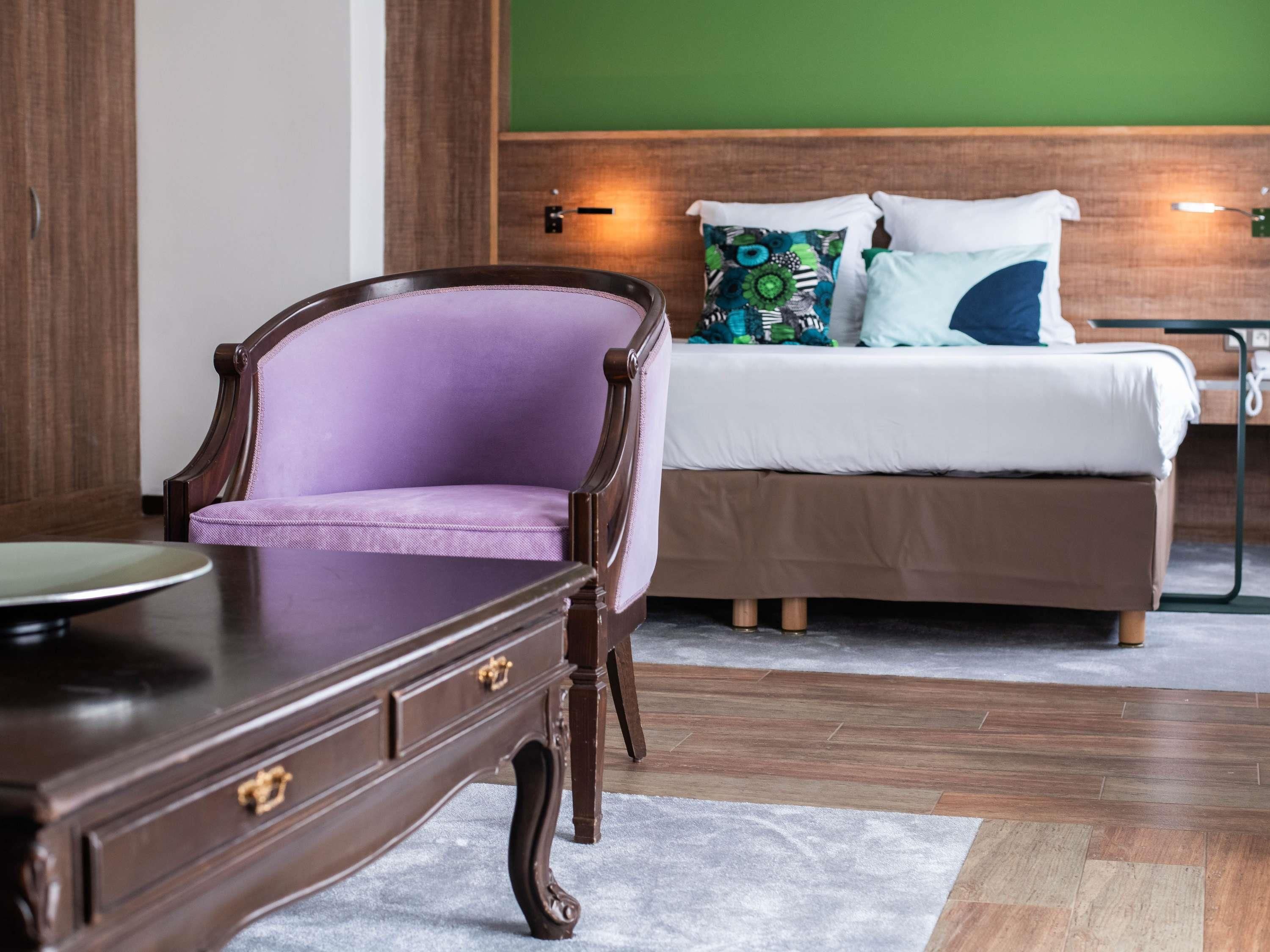 A bedroom with a wooden bed, a purple armchair, and a wooden nightstand.