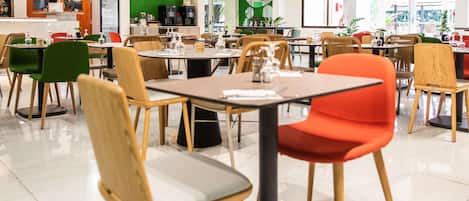 Un café amplio con varias mesas y sillas, una barra con un menú, y una pared verde.
