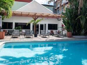 A poolside area with lounge chairs, a pergola, and a building with large windows. - Ibis Styles Cayenne Centre Amazonia (Ouverture Juin 2024) (Cayenne)