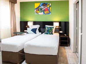 A hotel room with two single beds, a green accent wall, and a colorful artwork above the beds. - Ibis Styles Cayenne Centre Amazonia (Ouverture Juin 2024) (Cayenne)