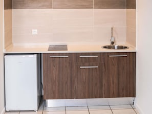 A compact kitchen with a built-in dishwasher, a stainless steel sink, and wooden cabinets. - Ibis Styles Cayenne Centre Amazonia (Ouverture Juin 2024) (Cayenne)