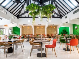 Um restaurante amplo com pé-direito alto, vegetação pendente e diferentes opções de assentos.