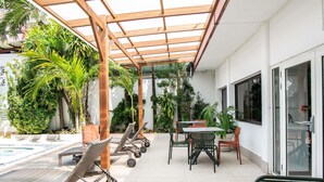 Un espacio al aire libre cubierto con sillones, una mesa y plantas en macetas.