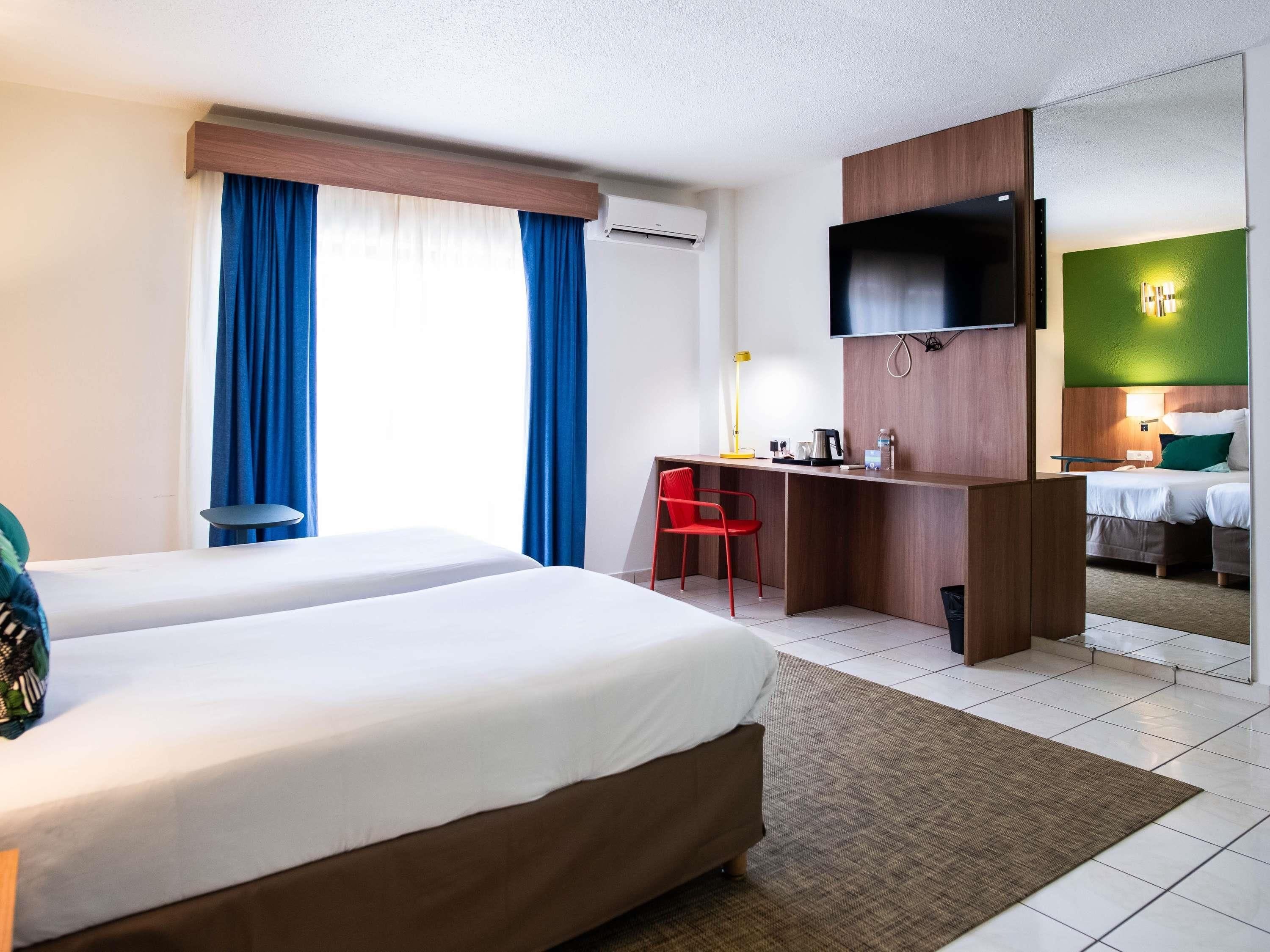 Une chambre d’hôtel avec deux lits, un bureau, une chaise, une télévision et un miroir.