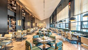 Um restaurante espaçoso com pé-direito alto, móveis modernos e grandes janelas que permitem a entrada de luz natural.