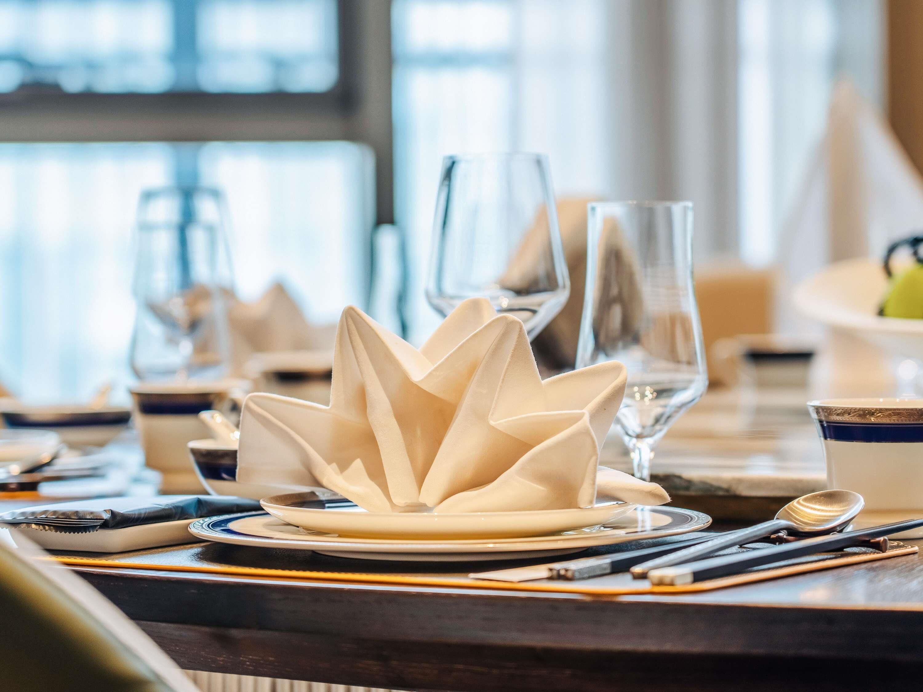 A dining table set with plates, cutlery, and a decorative lotus-shaped centerpiece.