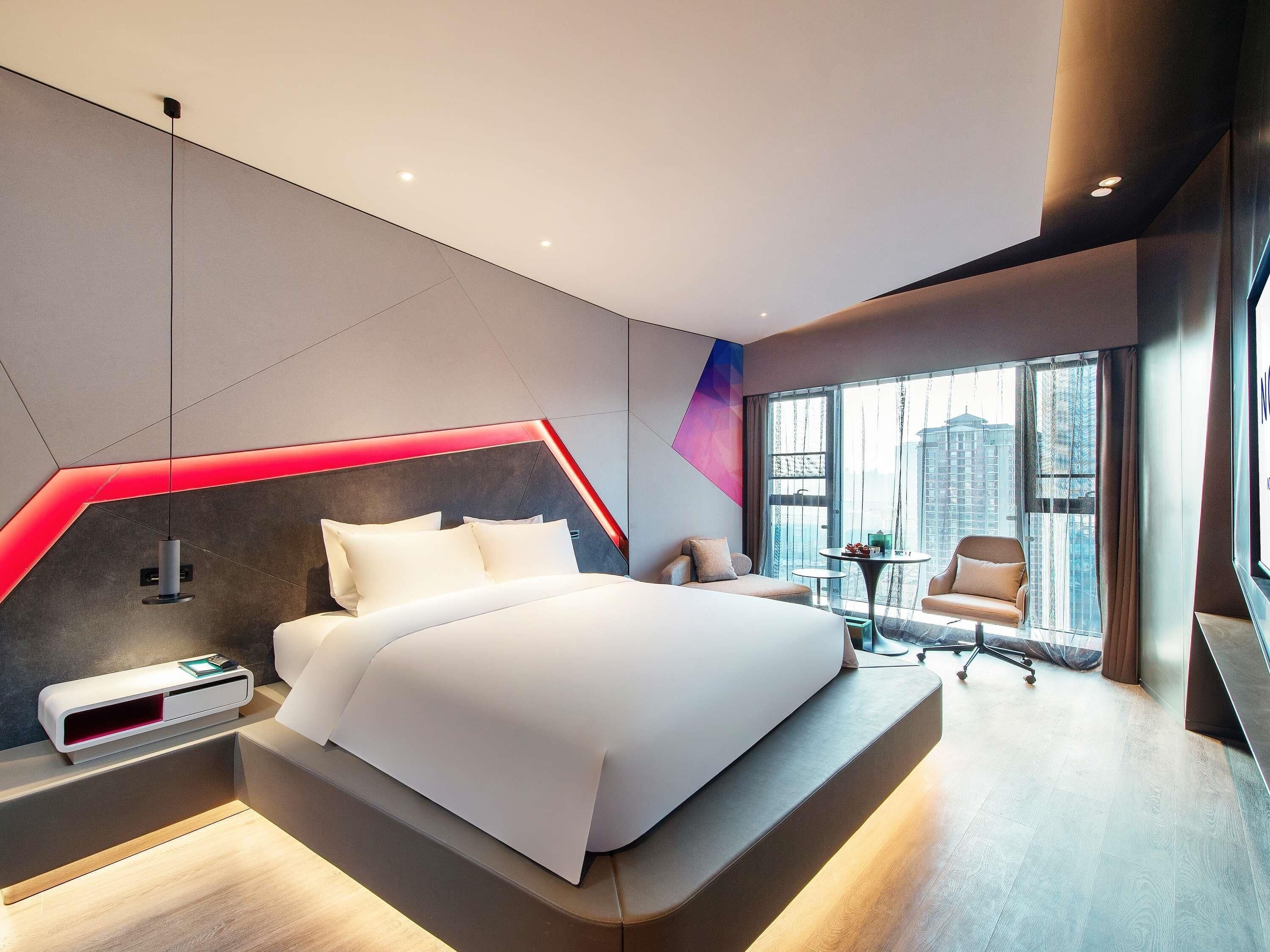 Habitación de hotel moderna con una cama grande, un escritorio, una silla y vistas a la ciudad.