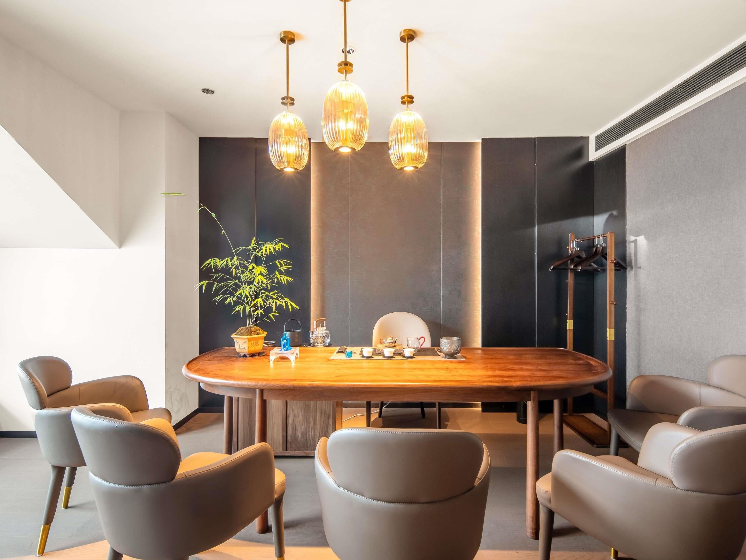 A modern dining area with a round table, leather chairs, a potted plant, and pendant lighting.