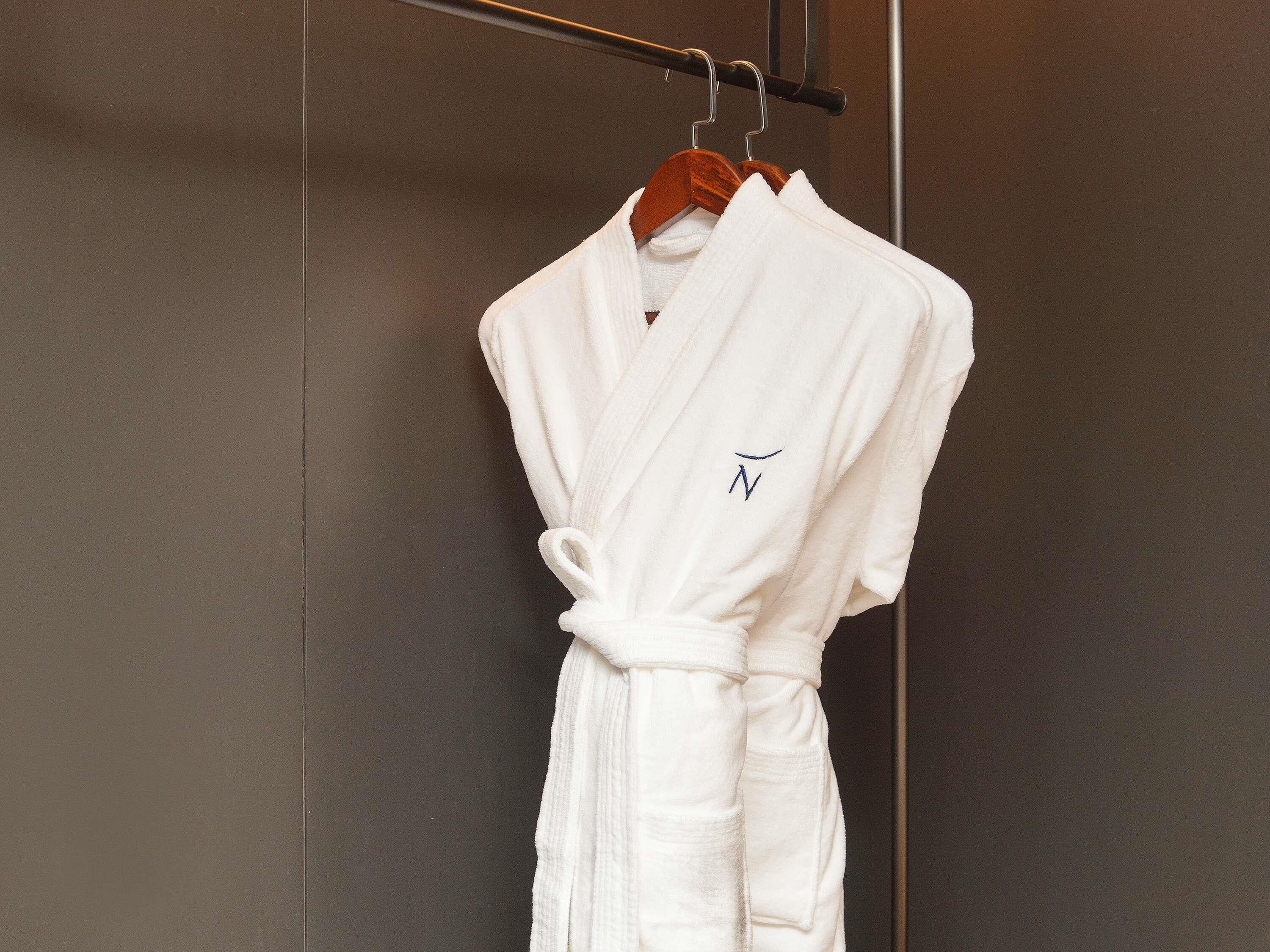 A white robe hanging on a wooden hanger in a bathroom with a dark wall.