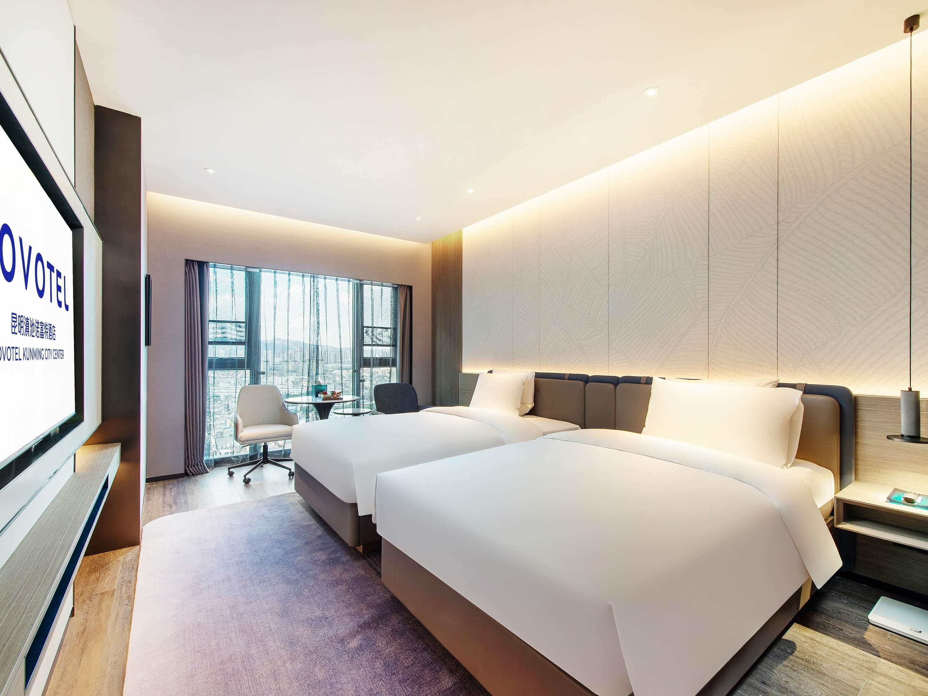 Een hotelkamer met twee bedden, een bureau, een stoel en een televisiescherm waarop de naam van het hotel staat.
