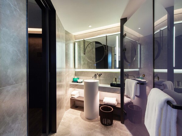 Un baño moderno con un espejo grande, un lavabo redondo y una cabina de ducha de vidrio.