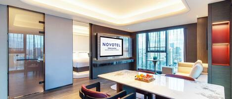 Ett modernt hotellrum med en stor TV, en matplats med bord och stolar samt utsikt över staden.