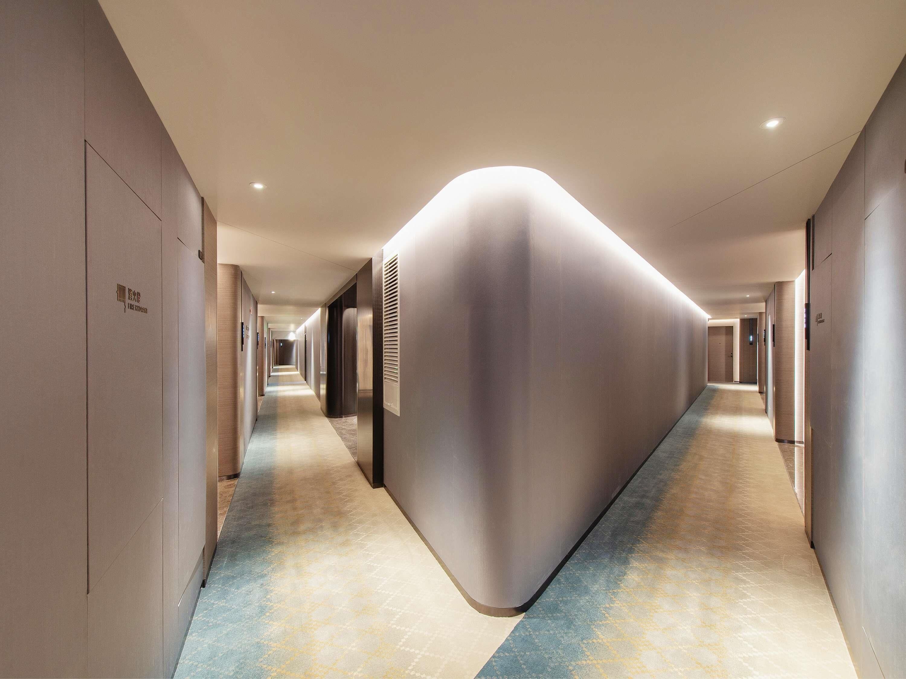 A modern hotel corridor with a curved wall, recessed lighting, and a patterned carpet.