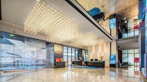 Um lobby moderno com piso refletivo, balcão de recepção e uma instalação de iluminação no teto.