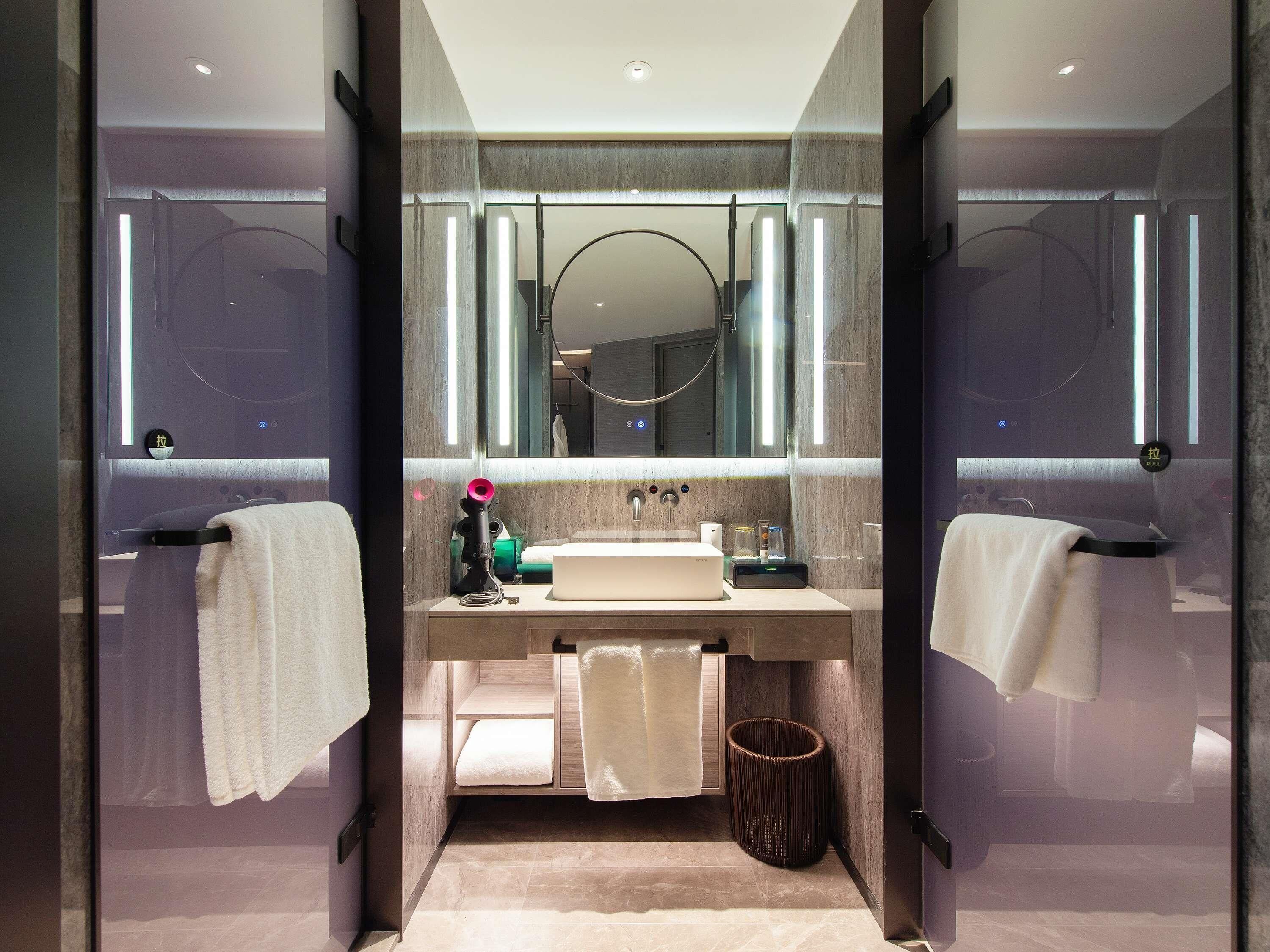 Un baño moderno con mampara de vidrio, lavamanos, espejo y perchero.