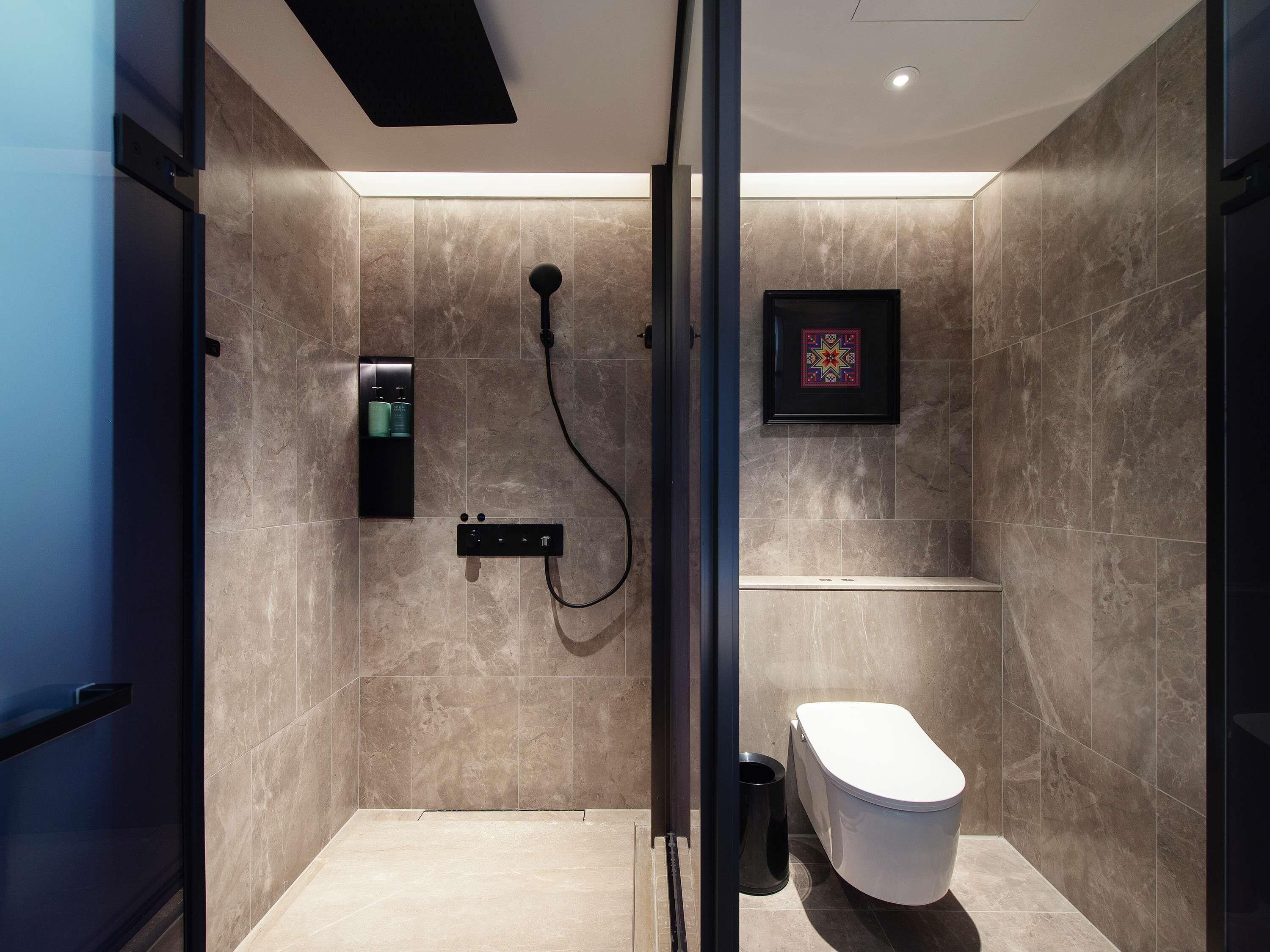 Un baño moderno con ducha, inodoro y un pequeño estante con artículos de aseo.