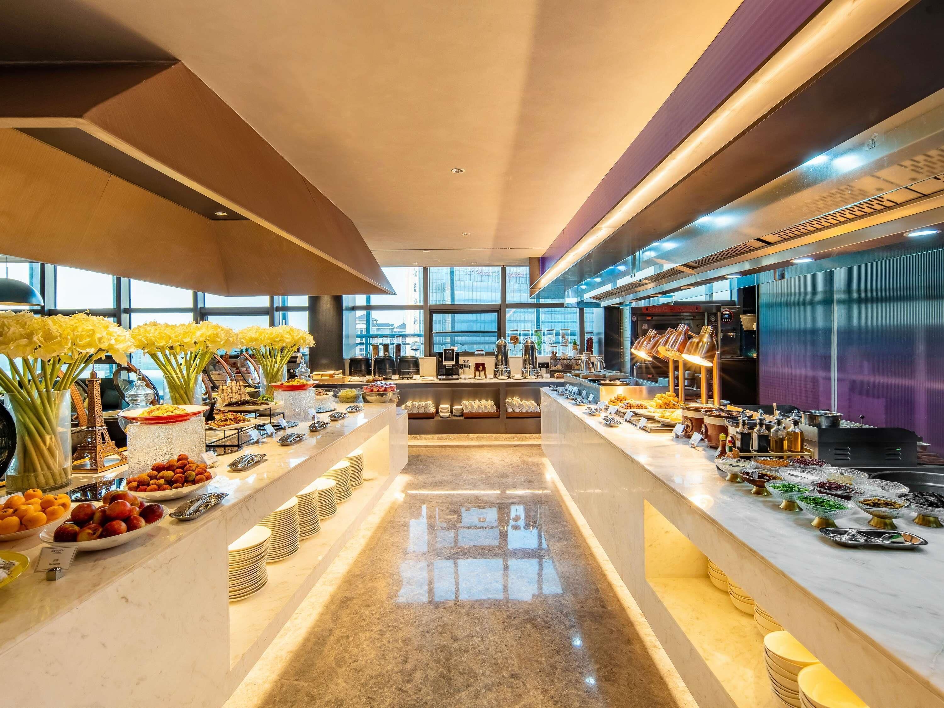 Een modern hotelontbijtbuffet met een centraal bedieningspunt, diverse drankdispensers en een uitzicht op de skyline door grote ramen.