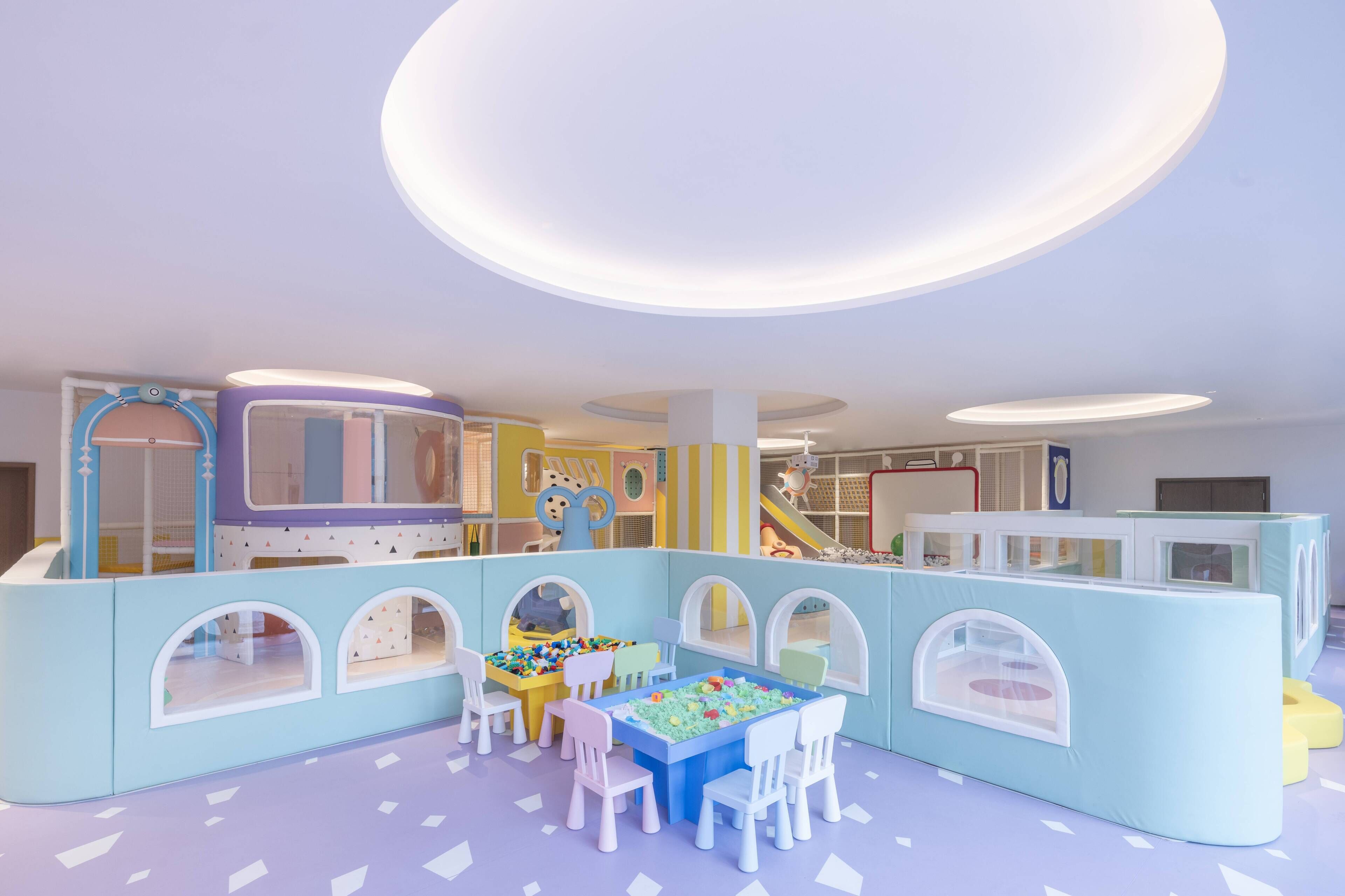 Zona infantil con una casita de juegos, mesas, sillas y un tobogán.