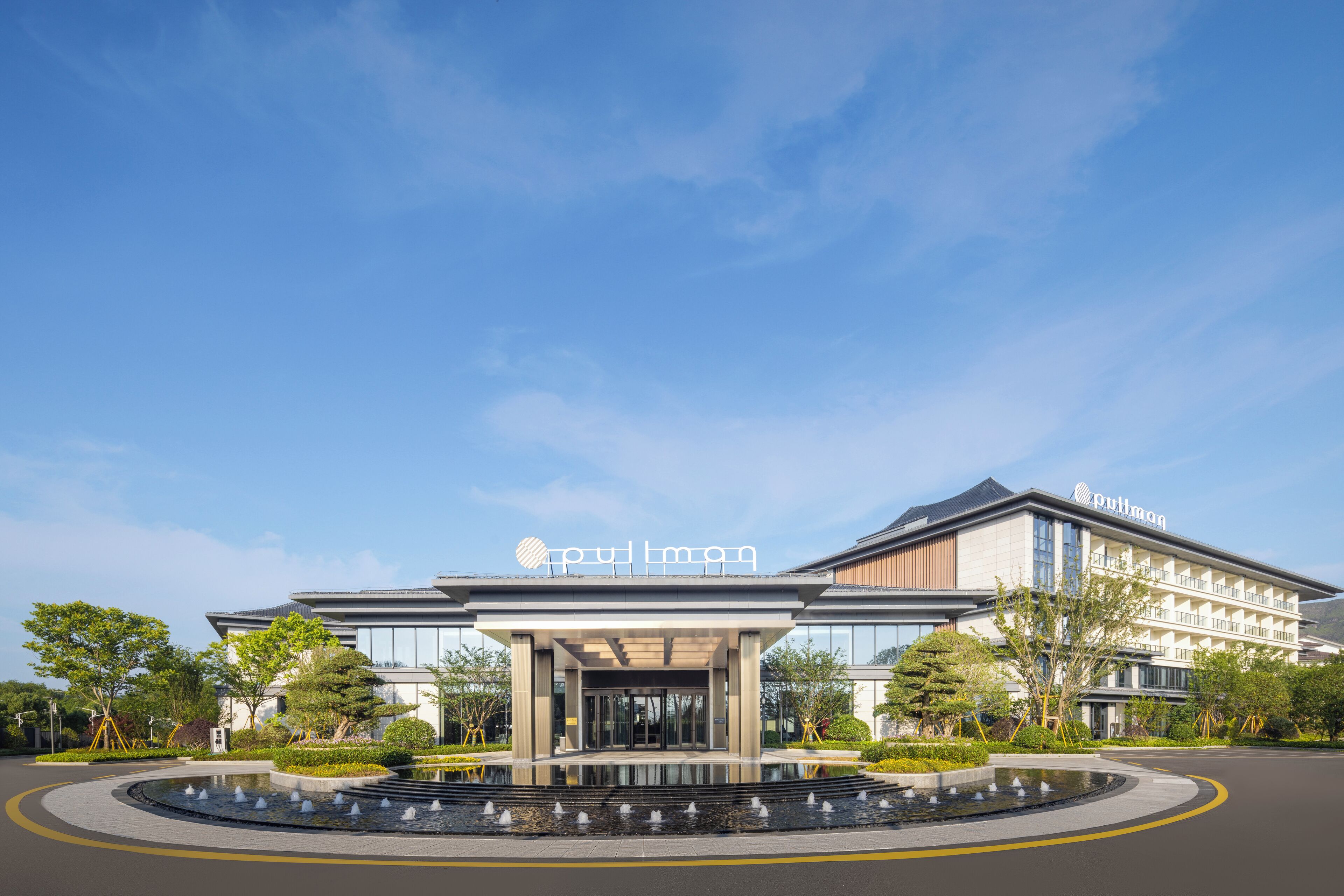 A hotel entrance with a modern design, a covered walkway, and a water feature in front.