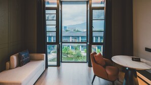 A modern hotel room with a large window, a sofa, a chair, and a small table. - Pullman Taizhou Shenxianju  (Taizhou)