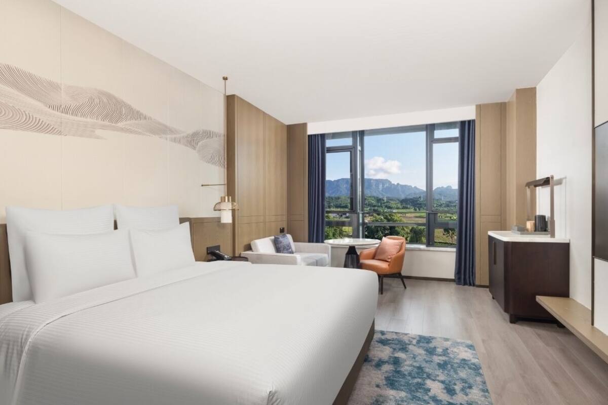 Ein modernes Hotelzimmer mit einem großen Bett, einem Schreibtisch, einem Sessel und Blick auf die Berge.