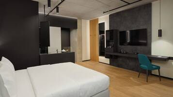 A modern hotel room with a large bed, a desk with a chair, a TV mounted on the wall, and a mirror above the desk.