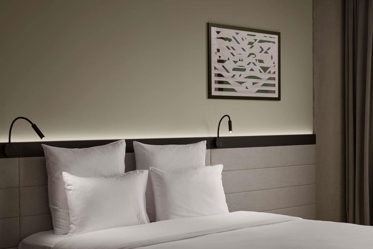 A neatly made bed with white linens, two bedside lamps, and a framed abstract artwork on the wall.