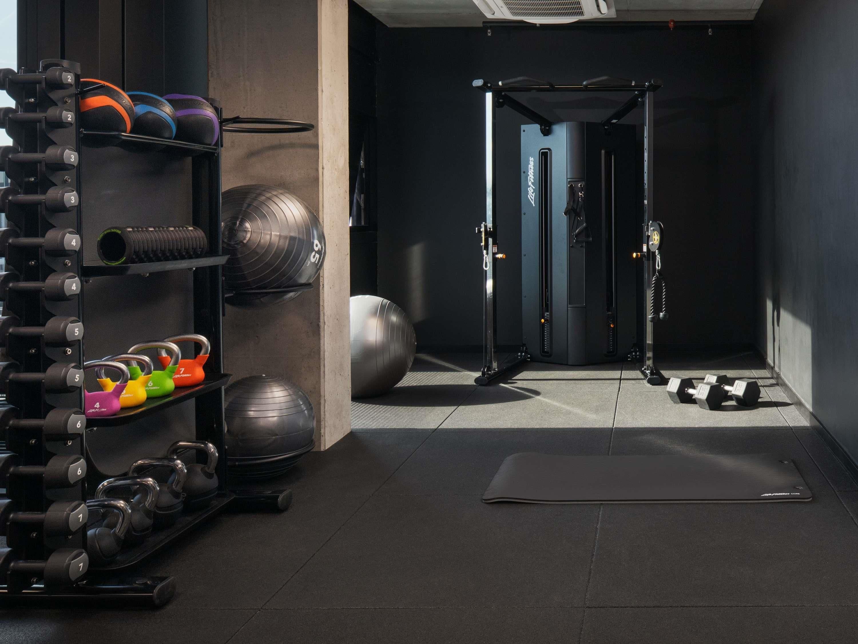 Ein Fitnessraum mit Gewichte, Trainingsbällen und einer Tür zu einem weiteren Raum.