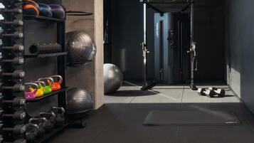 Ein Fitnessraum mit Gewichte, Trainingsbällen und einer Tür zu einem weiteren Raum.