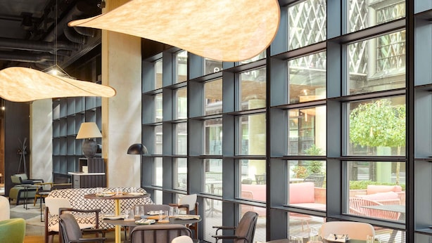 Un comedor moderno con mesas redondas, sillas y ventanas amplias que ofrecen vista a una terraza.