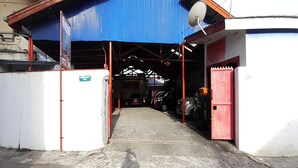 A covered parking area with a concrete floor, a red door, and a blue roof. - Hotel O Gurita Residence Syariah (Padang)