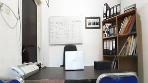 A small office with a desk, a laptop, a telephone, and a bookshelf. - Hotel O Gurita Residence Syariah (Padang)