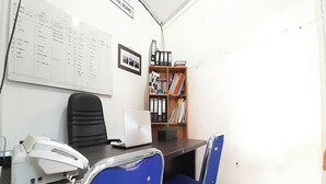 An office with a desk, a telephone, a laptop, a bookshelf, and a chair. - Hotel O Gurita Residence Syariah (Padang)