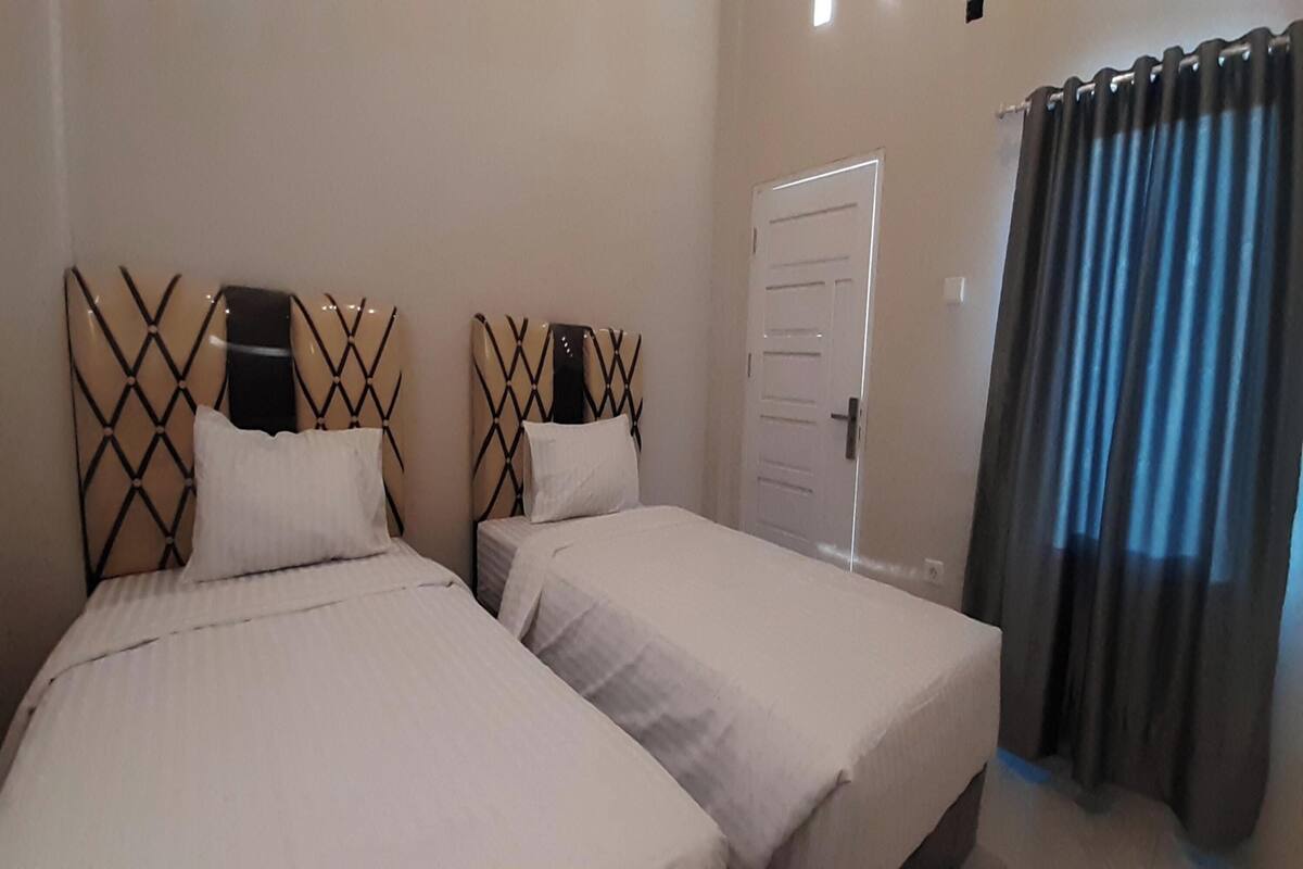 A room with two beds, each with a headboard featuring a geometric pattern. There is a door and a curtain on the right side.