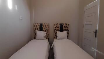 A small, compact room with two single beds, each with a unique headboard design.