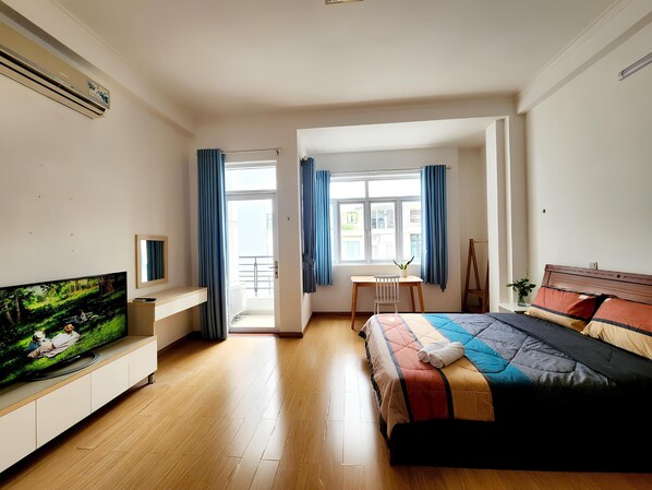 A modern bedroom with a large bed, a TV on a built-in shelf, a desk with a chair, and a window with curtains. - LaLaHouse Riverside Residence (Ho Chi Minh City)