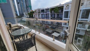 A balcony with a glass table and chairs, overlooking a street with buildings and a restaurant. - LaLaHouse Riverside Residence (Ho Chi Minh City)