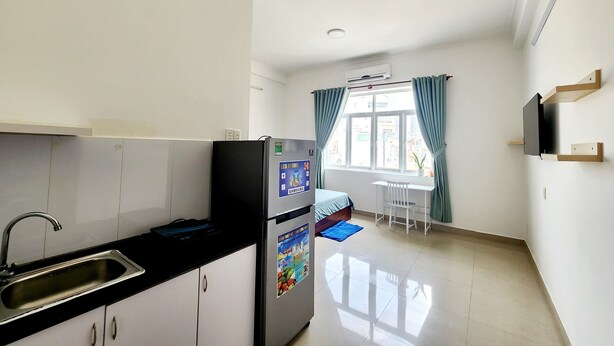 A compact kitchen with a refrigerator, sink, and a window with curtains. - LaLaHouse Riverside Residence (Ho Chi Minh City)