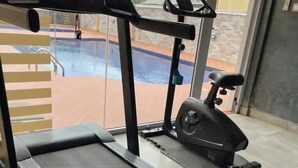 Un gimnasio con una cinta de correr, una elíptica y una piscina visibles a través de puertas de vidrio.