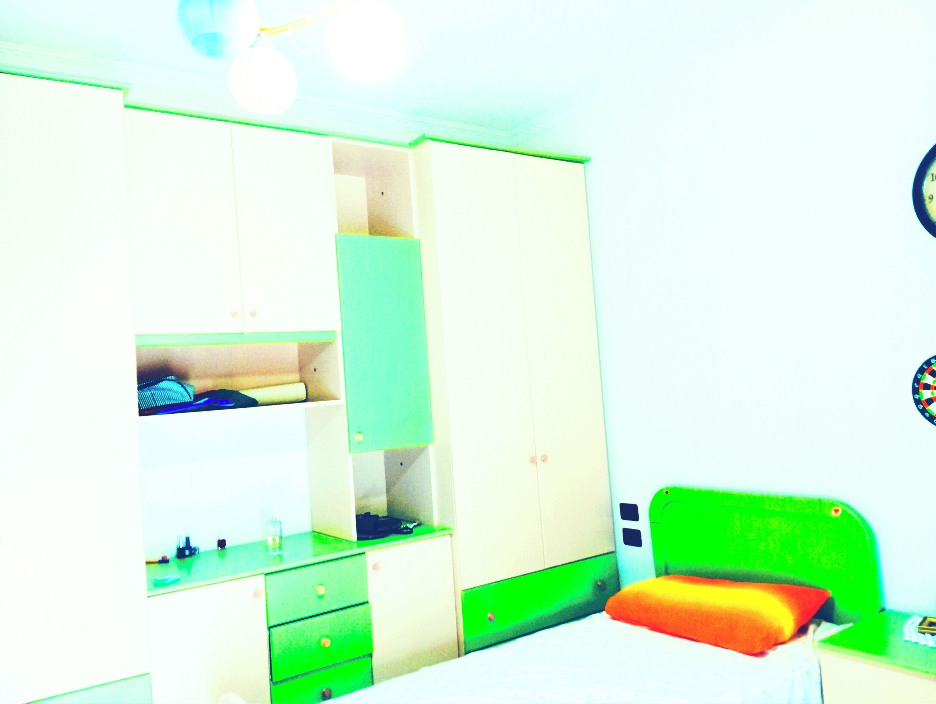 Une chambre avec un lit, une tête de lit verte, une armoire et un miroir.