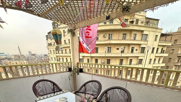 A rooftop terrace with a glass table and wicker chairs, overlooking a cityscape. - LUNA HOTEL (Cairo)