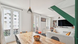 Un salon moderne avec une table à manger en bois, un canapé gris et un téléviseur fixé au mur.