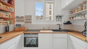 Une cuisine moderne avec des armoires blanches, des comptoirs en bois, un four encastré, un évier et une fenêtre donnant sur la ville.