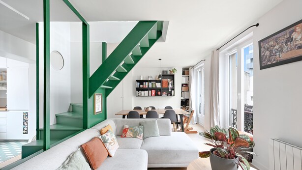 Un salon moderne avec un escalier vert, un coin repas et une grande fenêtre.