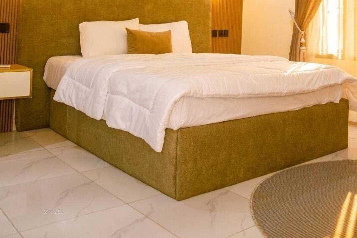 Una habitación de hotel moderna con una cama grande, panel de madera y luz ambiental.