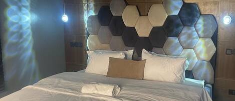 A modern bedroom with a hexagonal headboard, a bed with white linens, and an air conditioning unit mounted on the wall.