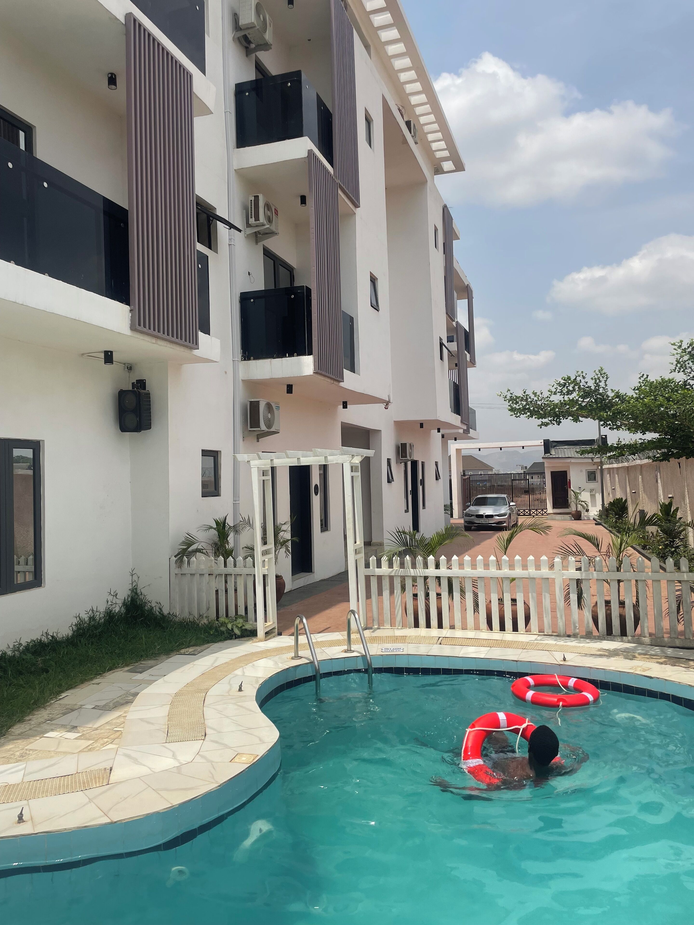 A residential building with a swimming pool, white picket fence, and a parked car.